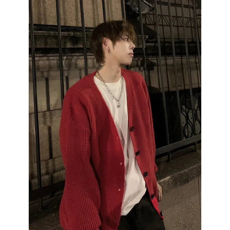 A man's loose-fitting V-neck knitted cardigan in a solid colour on a hanger.