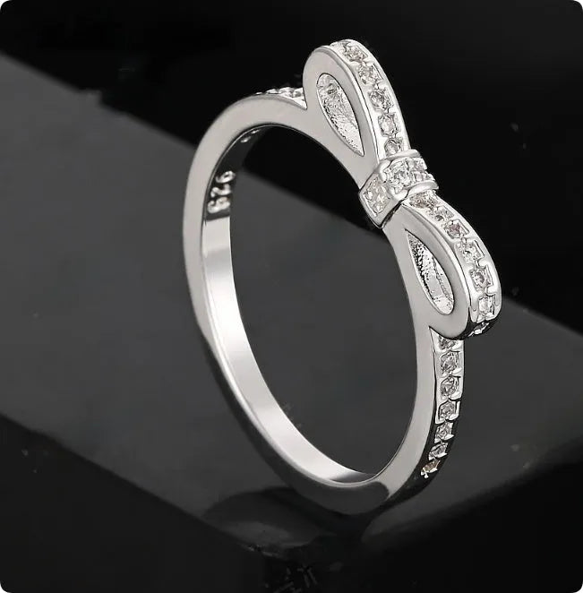 Silver-coloured bow-shaped ring with sparkling zircon crystal stones on a finger.