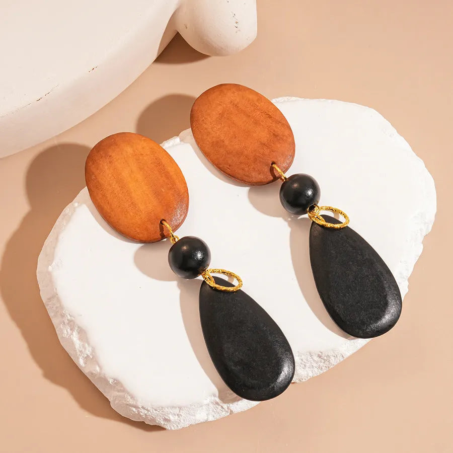 Handcrafted brown and black wooden elliptical earrings with silver needle detail on a retro style background.