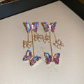 Silver toned earrings with a blue purple butterfly, crystal flowers, and a long tassel drop chain.