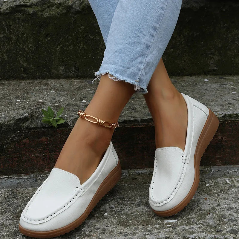 Women's flat slip-on loafers in PU leather with car stitch detail and a round toe, shown on a white background.