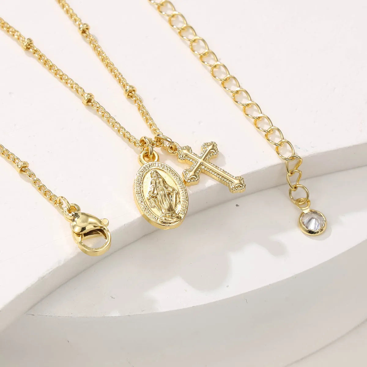 Gold Virgin Mary cross necklace with simple geometric pendant on a chain.