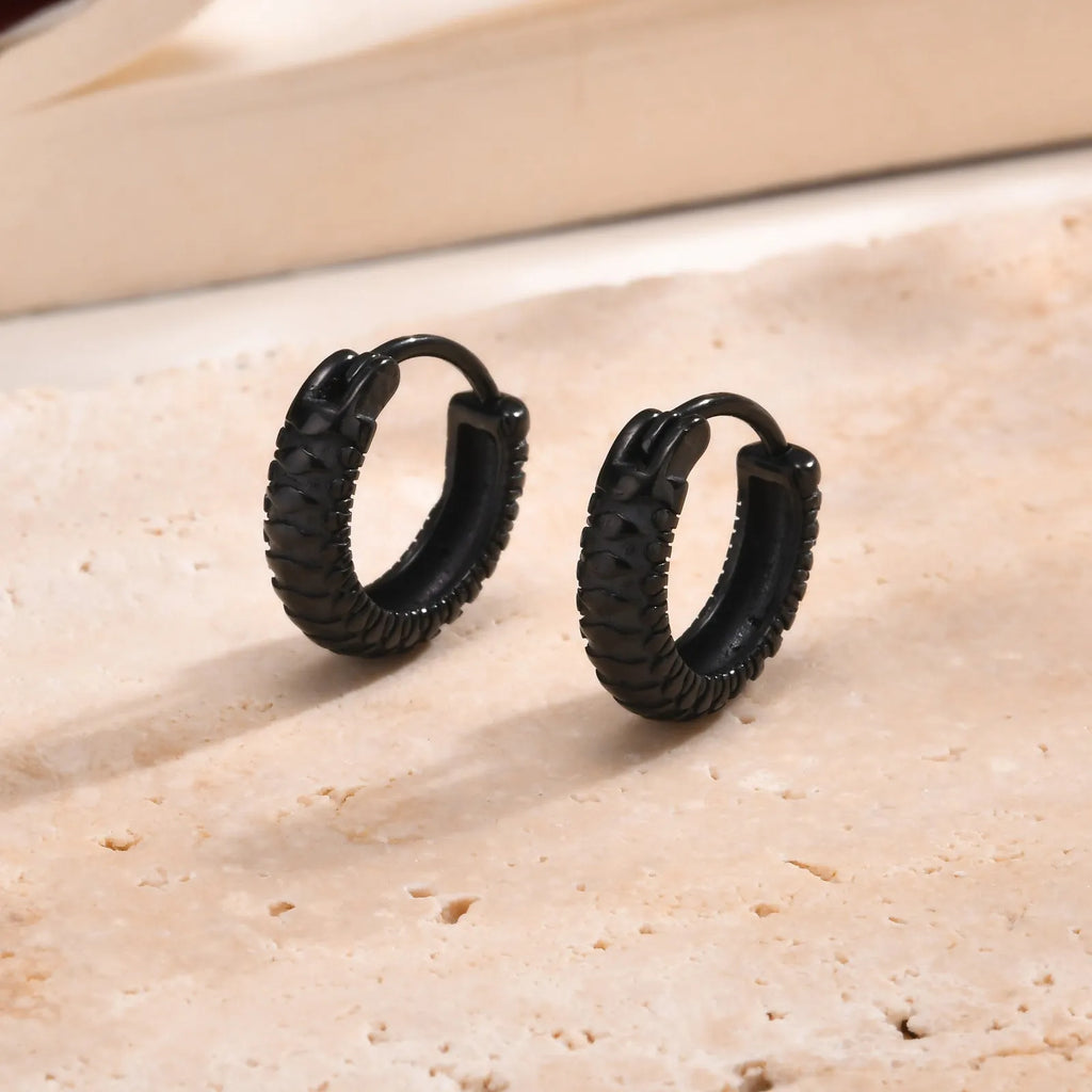 A pair of stainless steel earrings with a raised snake pattern texture in a black or gold finish.