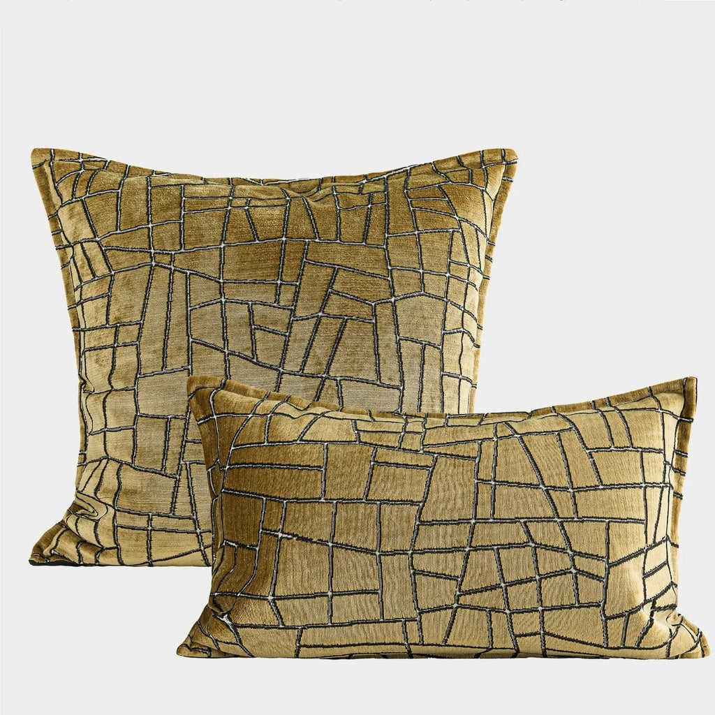 Gold geometric pattern on a velvet square cushion and a rectangular waist pillow against a sofa.