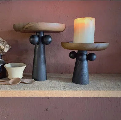 Round wooden tray with high Nordic-style legs in a light wood finish holding a candle