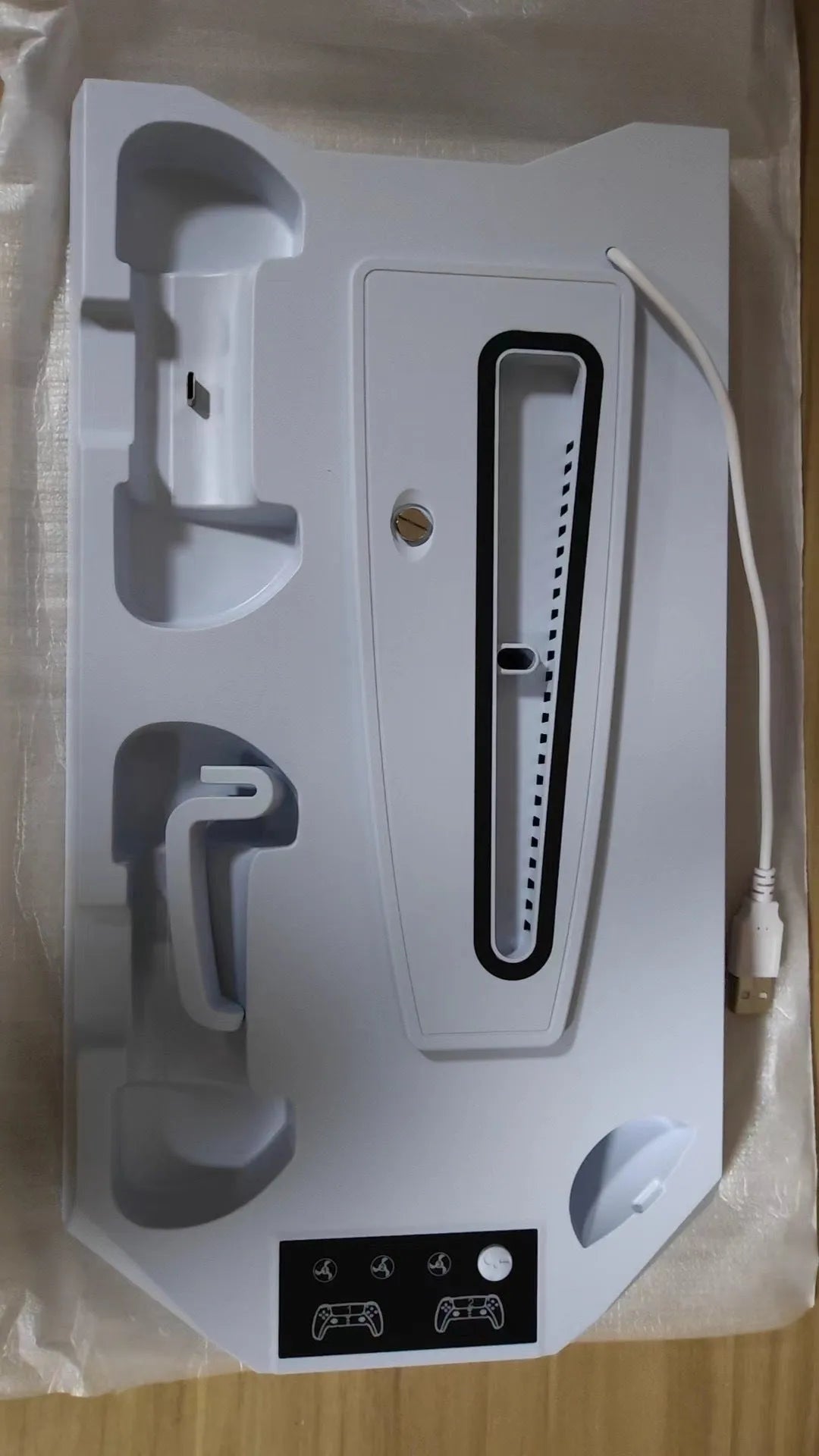 White PS5 charging stand with console upright, DualSense handle docked, and headset on hook.