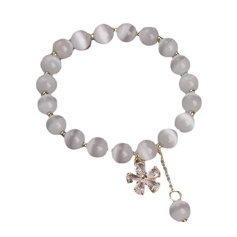 Women's white cat's eye bracelet with flower tassel and safety buckle pendant on wrist