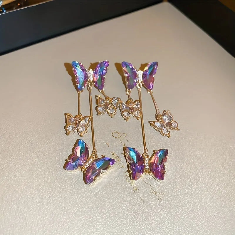 Silver toned earrings with a blue purple butterfly, crystal flowers, and a long tassel drop chain.