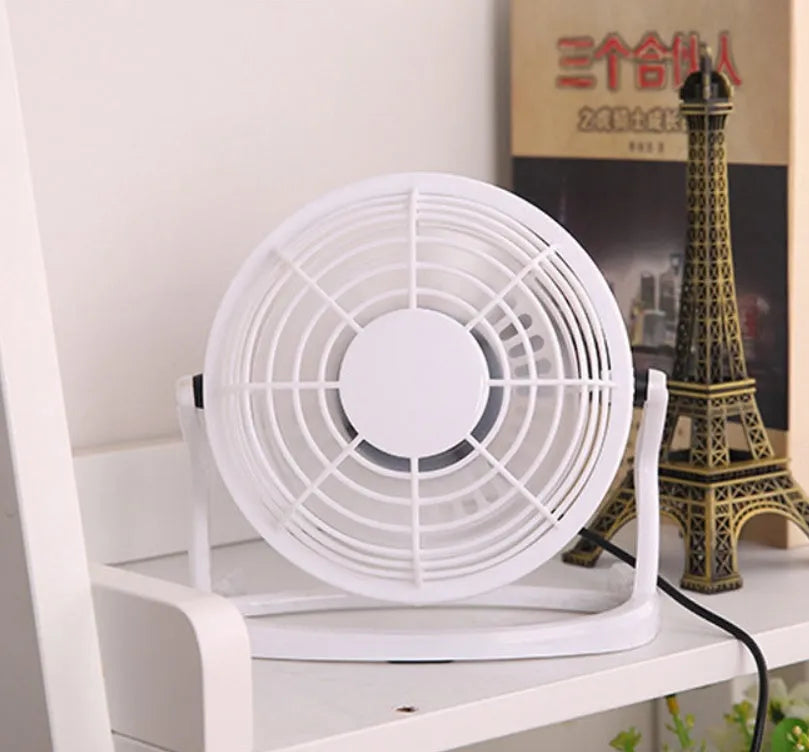Compact black mini USB desk fan with adjustable tilt, placed next to a laptop.