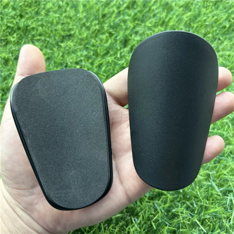 Pair of extra small black and white plastic football shin guards, size 8x5cm.