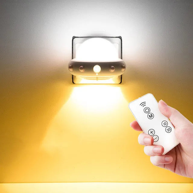Remote control UFO shaped bedside night light in blue, pink, or white on a bedside table.