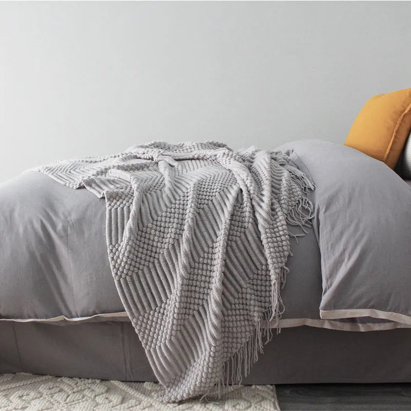 Small grey polyester nap blanket folded on a sofa, showing its texture and size.