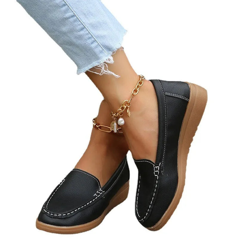 Women's flat slip-on loafers in PU leather with car stitch detail and a round toe, shown on a white background.