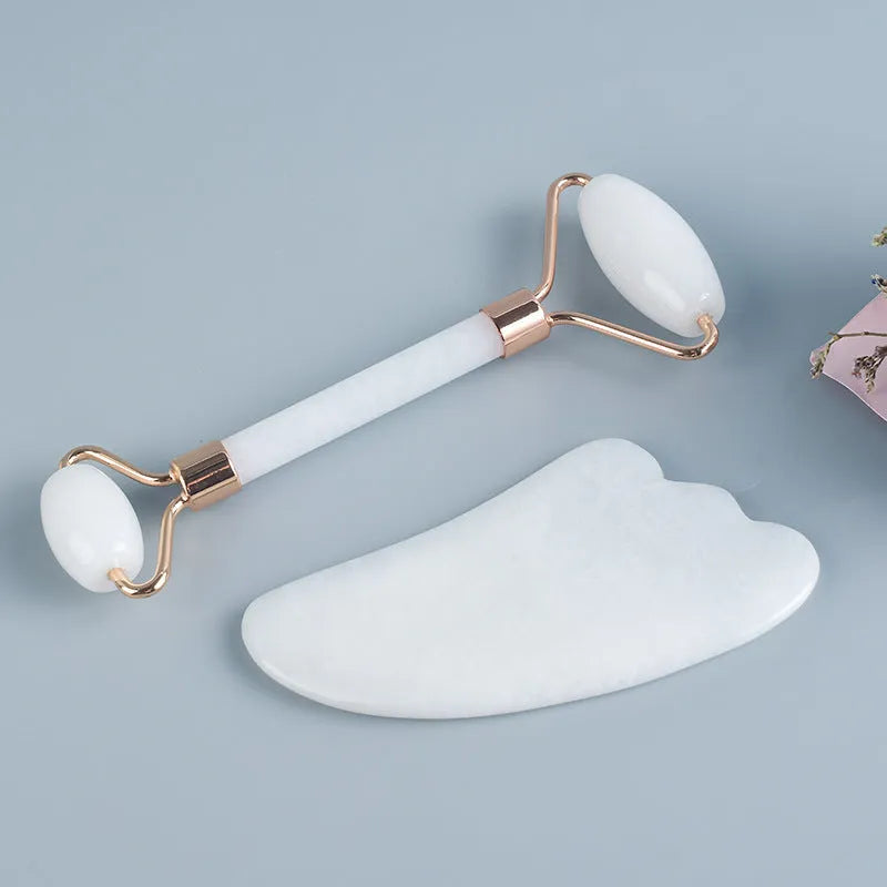 White jade double-headed facial roller and scraping board set on a plain surface.