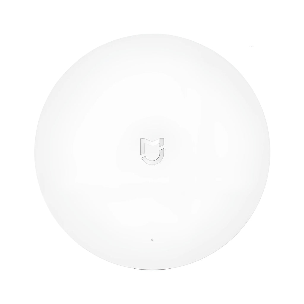 White circular Xiaomijia smart home gateway hub with UK plug on a table.