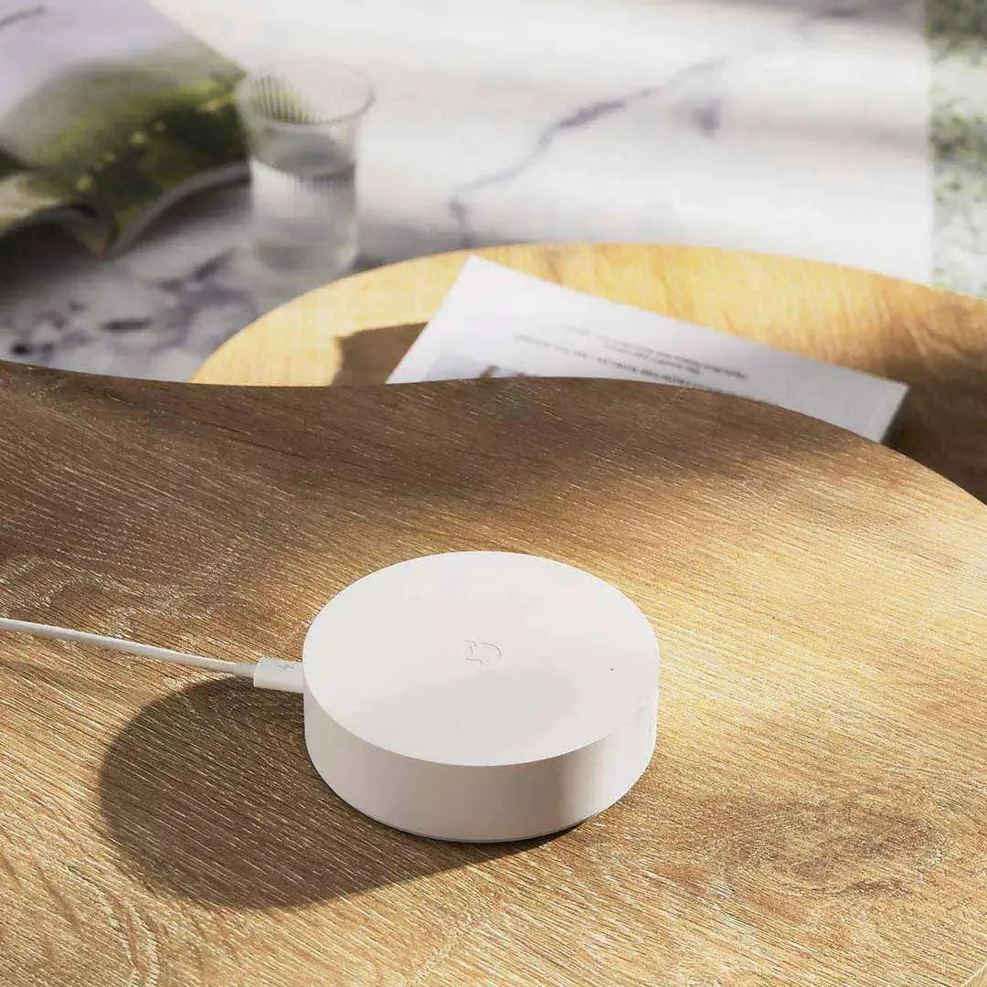 White circular Xiaomijia smart home gateway hub with UK plug on a table.