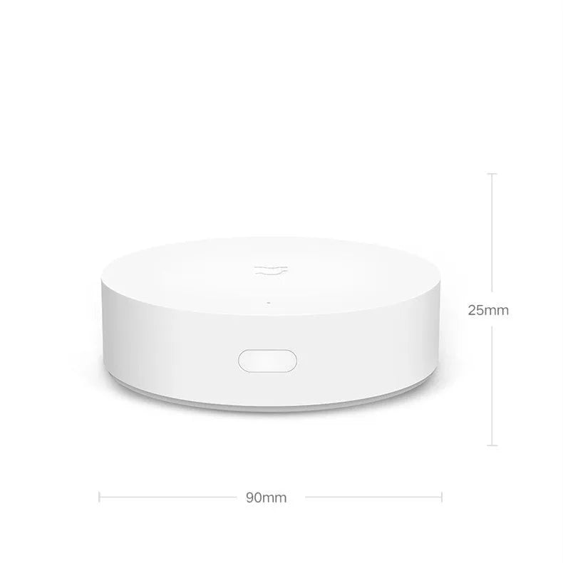 White circular Xiaomijia smart home gateway hub with UK plug on a table.