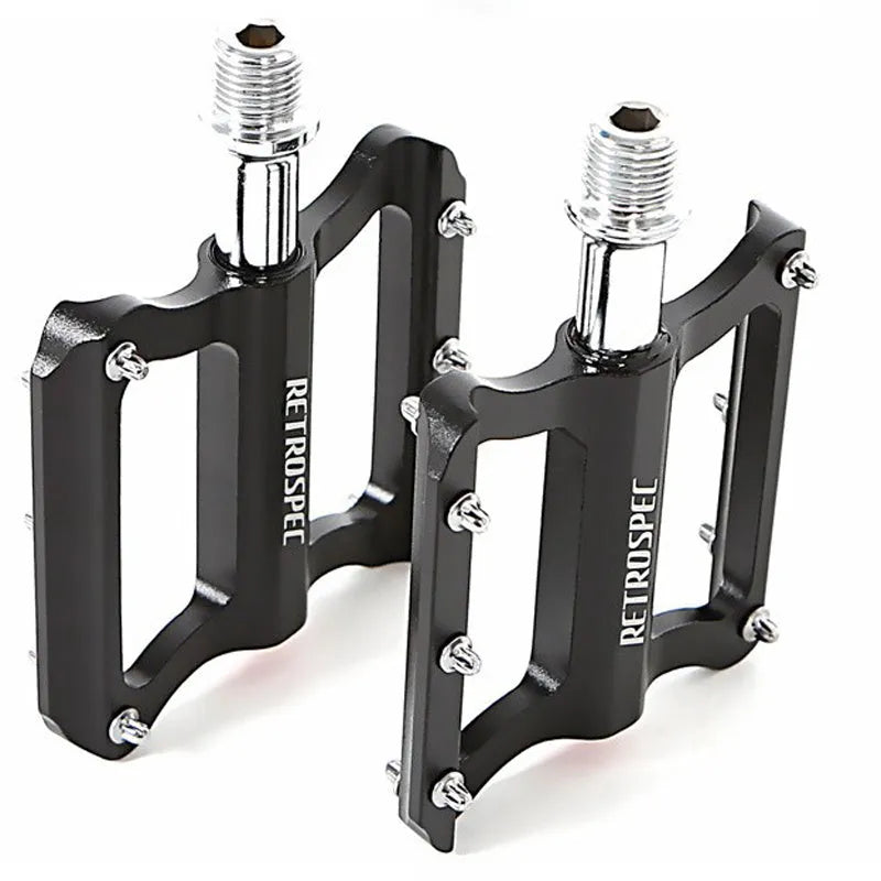 Pair of black CNC aluminium mountain bike pedals with sealed bearings and anti-skid nails on a white background