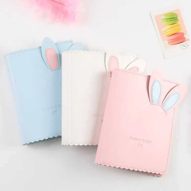 Small pink loose-leaf photo album with rabbit-themed pages, shown next to a 3-inch photograph for scale.