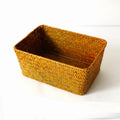 Natural woven straw storage box on a wooden desk, holding pens and cosmetic bottles.