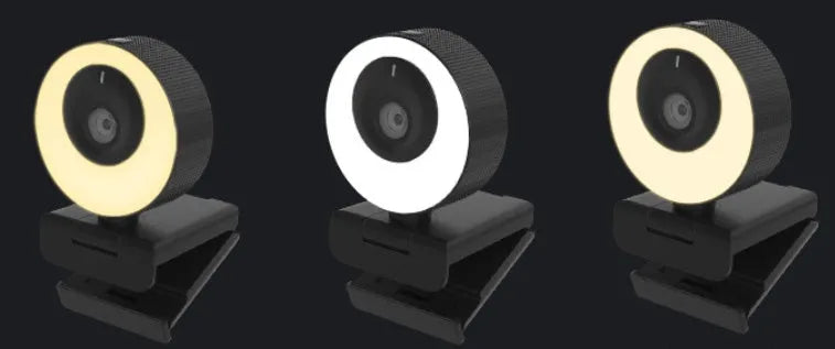 Black USB webcam with a magnetic privacy cover on a desk next to a laptop.