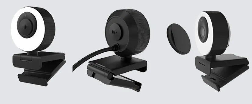 Black USB webcam with a magnetic privacy cover on a desk next to a laptop.