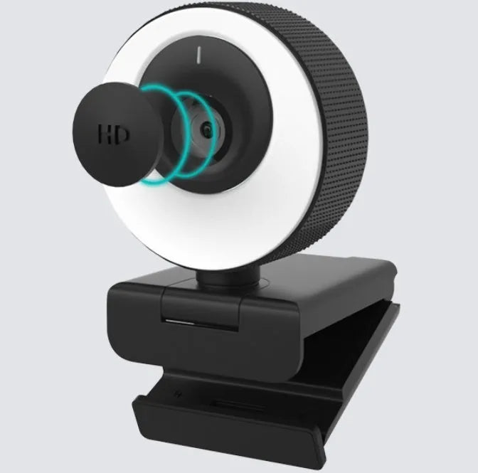 Black USB webcam with a magnetic privacy cover on a desk next to a laptop.