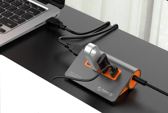 Dark grey and orange aluminium USB-C hub with four USB 3.1 ports, a DC power input, and a detachable cable.