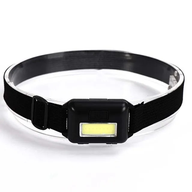 Compact black LED headlamp with a fabric head strap, shown in use.