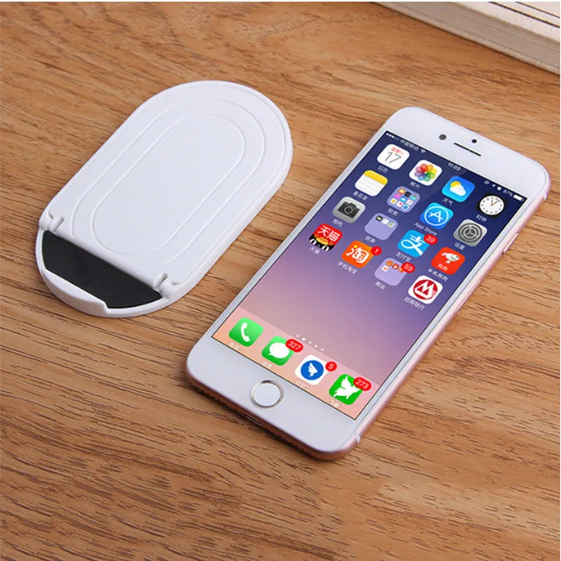 Plastic lazy bracket mobile phone stand in six colour options on a desk.