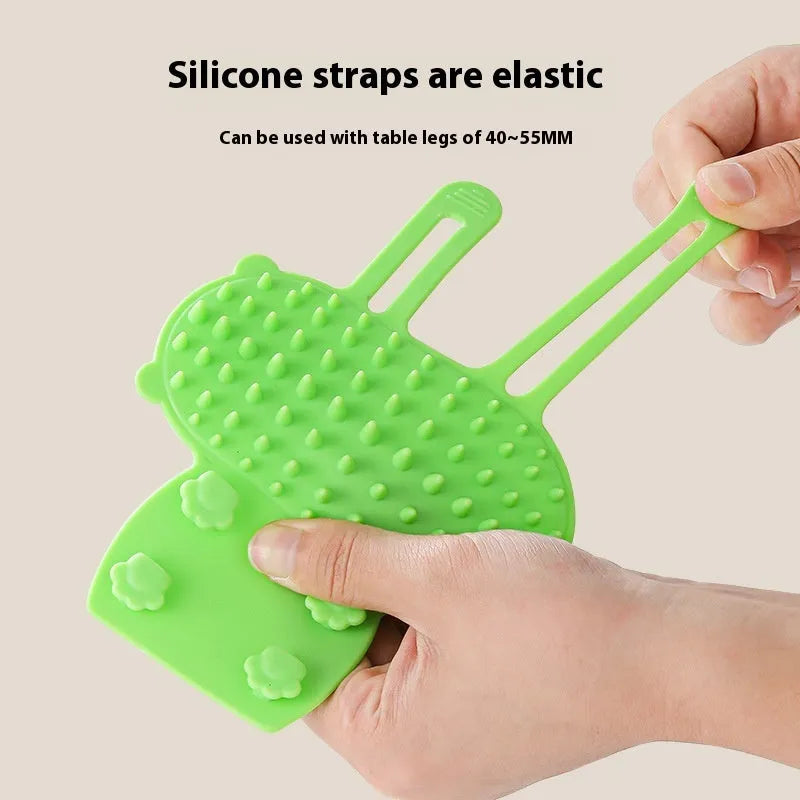 Silicone cat grooming comb with adjustable strap mounted on a table leg, shown in green colour.