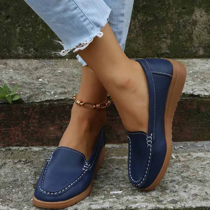 Women's flat slip-on loafers in PU leather with car stitch detail and a round toe, shown on a white background.