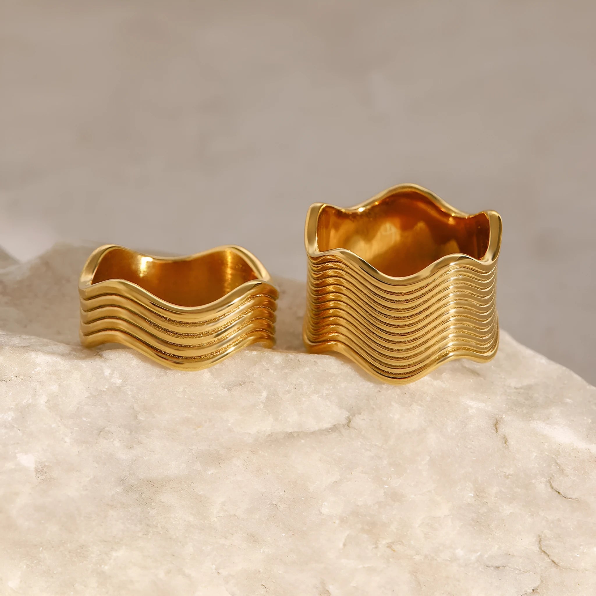Stainless steel women's ring with a wide geometric wave surface design in a silver or gold finish.