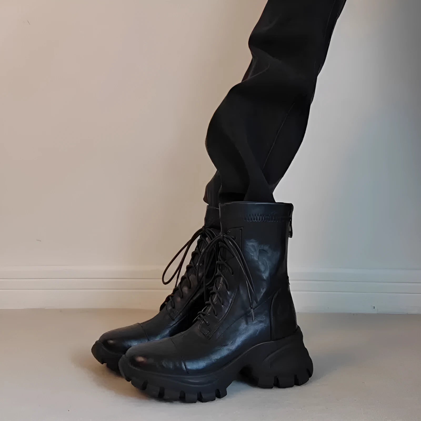 Black thick-soled motorcycle boots with back zipper and lace-up closure on a grey background