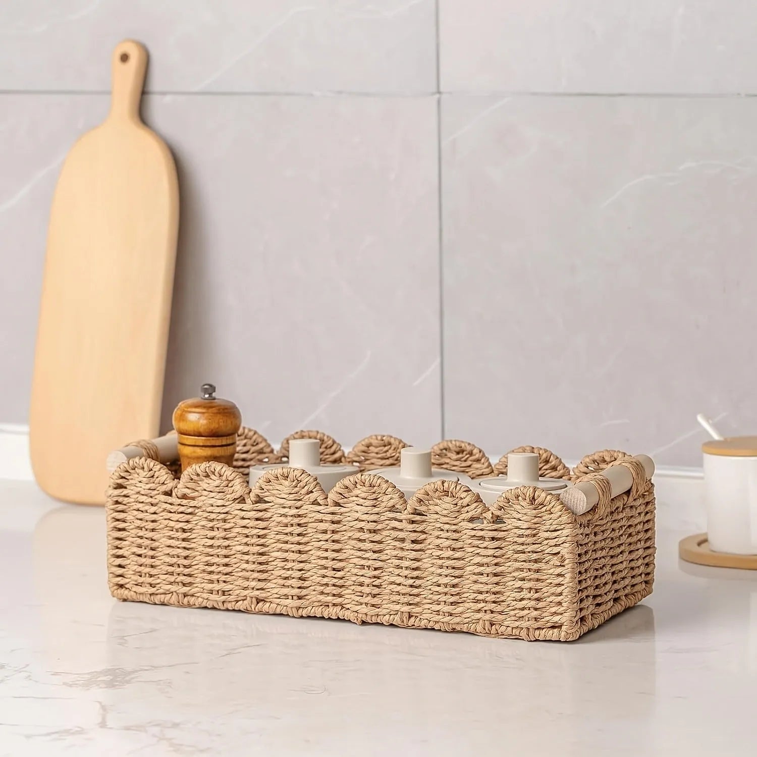 Modern woven paper storage basket in khaki colour on a wooden desktop, holding remote controls and pens.