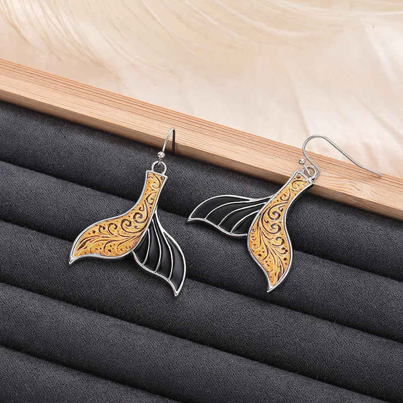 A pair of gold-coloured alloy fishtail earrings with a detailed whale tail design on post studs.