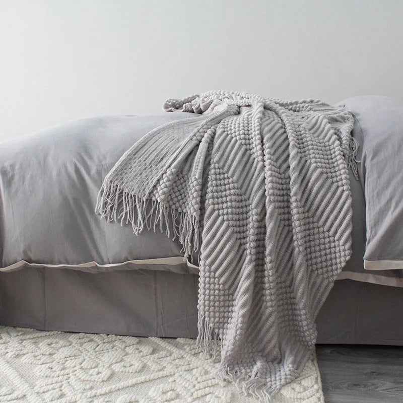 Small grey polyester nap blanket folded on a sofa, showing its texture and size.