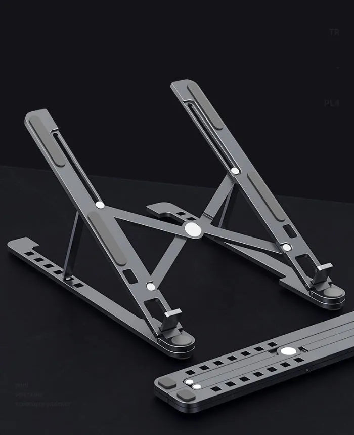 A folded silver aluminium laptop stand next to an open laptop, showing its thin profile and adjustable angle mechanism.