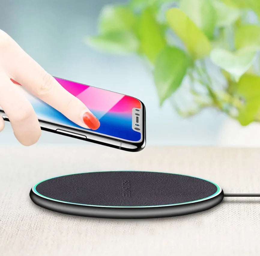 Black Qi wireless charging pad for iPhone 11 placed on a wooden surface.