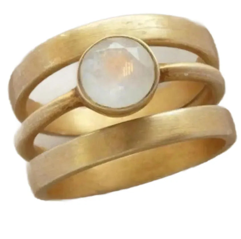 A gold geometric ring with linear design and a micro-inlaid white chalcedony stone on a grey background.