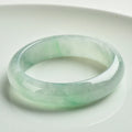 A light green jade bracelet for men and women, shown on a wrist, with a natural stone texture.