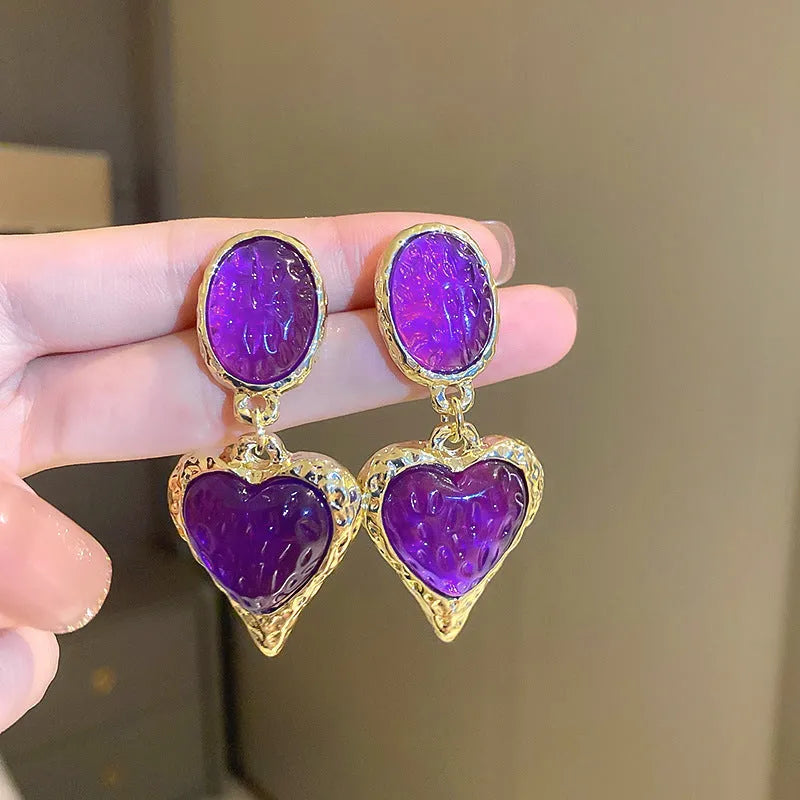 A pair of alloy silver needle pleated oval love heart stud earrings on a purple background.
