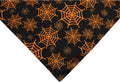 Black and orange reversible Halloween dog bandana with pumpkin and spider web patterns laid flat.