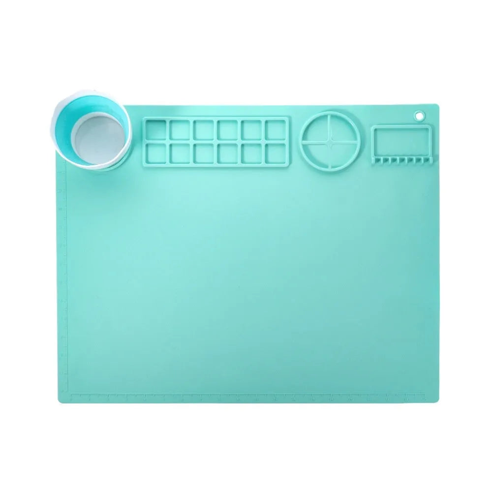 Light blue silicone painting mat with an integrated bowl on one side, positioned on a wooden table.