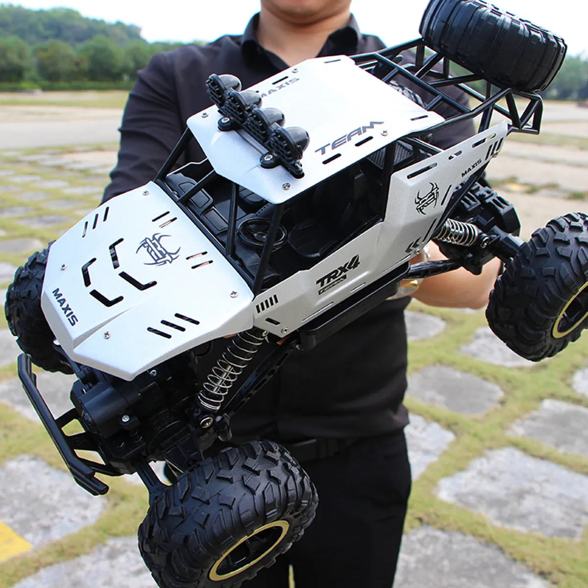 Large black or silver 4WD remote control climbing car on off-road terrain with wireless remote.