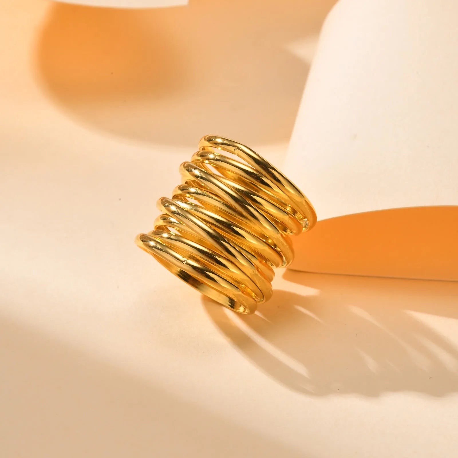 Gold stainless steel multi-loop multi-layer ring on a plain background