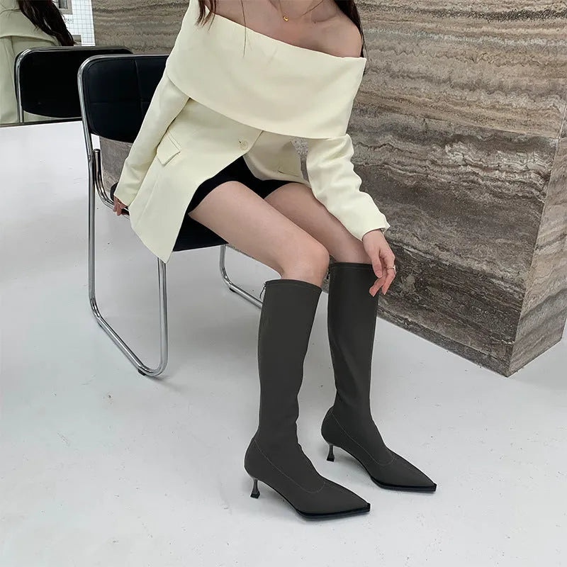 Black pointed toe knee-high boots with a stiletto heel and back zipper, shown on a model