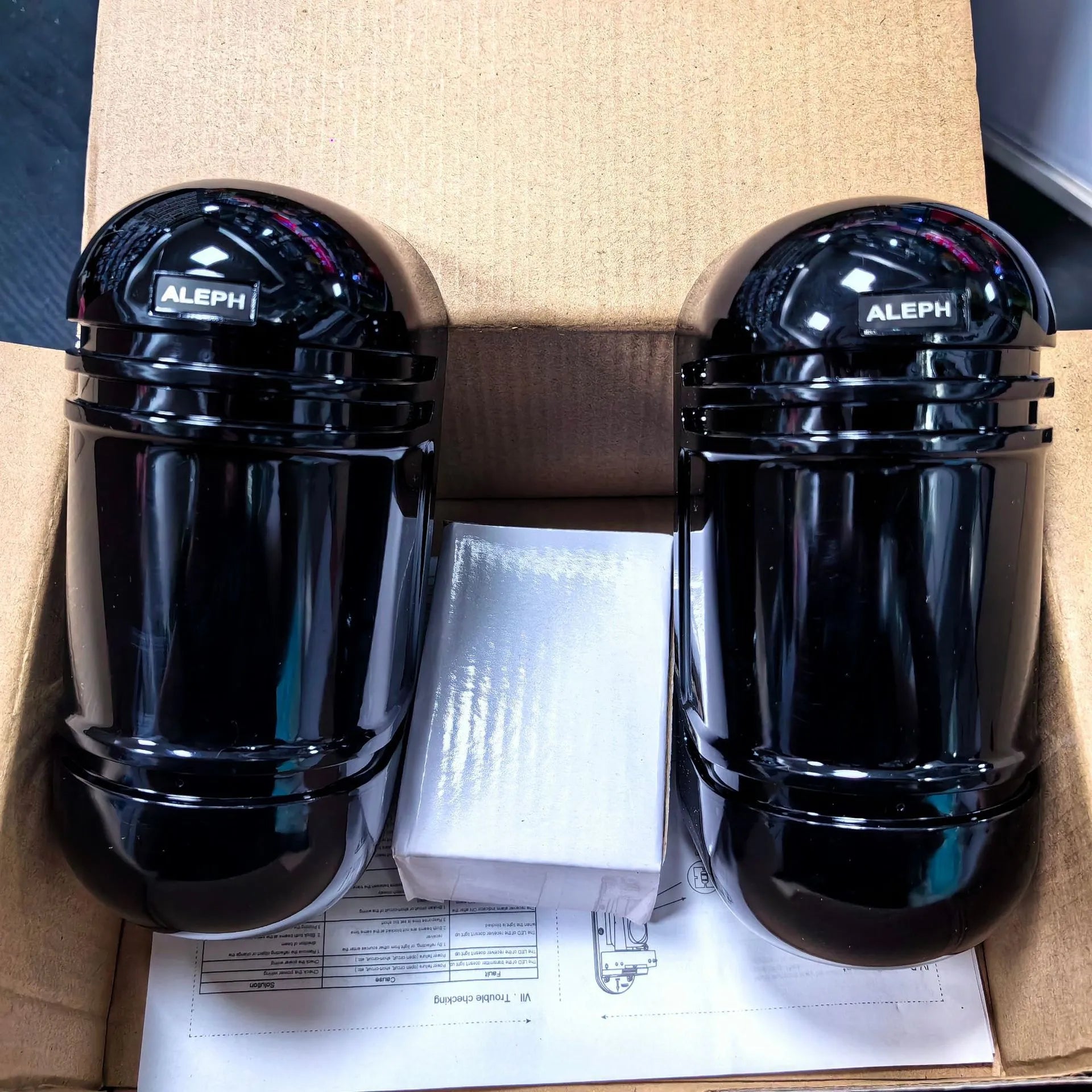 A pair of black wall-mounted infrared security detectors with wired terminals.