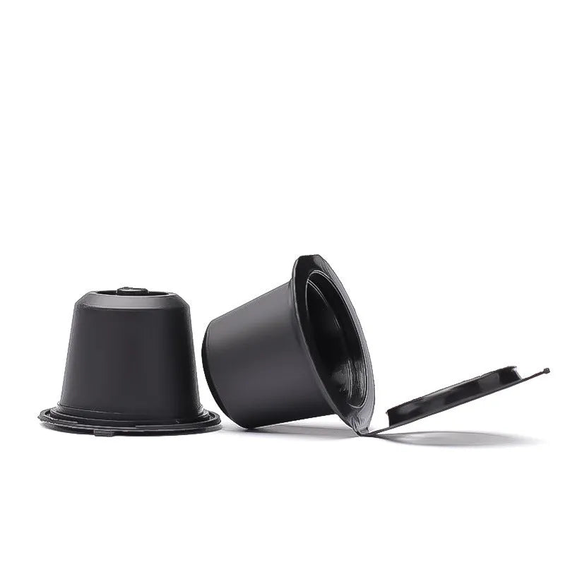 Six reusable black plastic coffee capsule filter cups with a spoon on a table