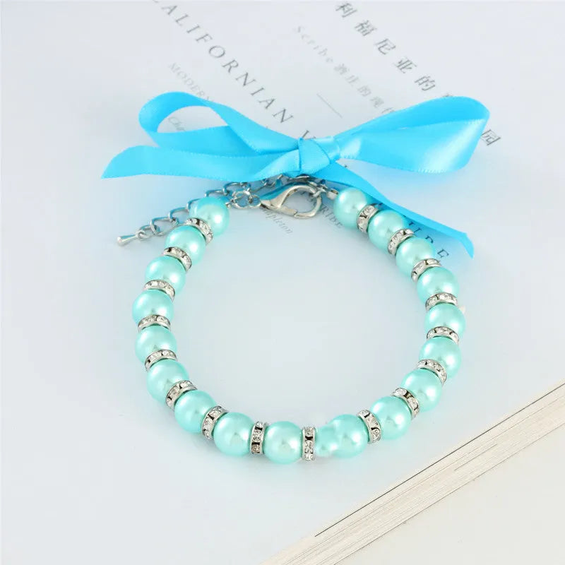Adjustable blue pearl and rhinestone dog necklace collar with ribbon bow on a small dog.